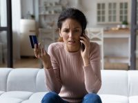 Eine Frau ist wütend während sie telefoniert und eine Bezahlkarte in der Hand hält.