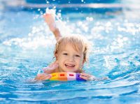 Ein Kleinkind paddelt fröhlich mit einer Schwimmhilfe durch das Wasser.