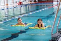 Ein Mädchen und ein Junge üben schwimmen mit zwei Schaumstoff-Hilfen.