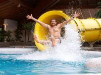 Ein junger Mann rutscht aus der Wasserrutsche im Hildorado heraus und breitet begeistert die Arme aus.