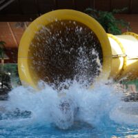 Wasser spritzt hoch auf, als eine Person aus einer großen Wasserrutsche herauskommt.