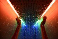 Hände strecken sich nach oben in der in bunten Farben beleuchteten Regendusche.