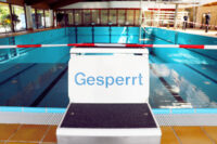 Ein Schild mit der Aufschrift "Gesperrt" steht auf einem Sprungblock am Schwimmerbecken des Hildorado. Im Hintergrund ist rot-weißes Absperrband gespannt.