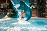 Ein Junge rutscht von einer großen blauen Wasserrutsche in ein Becken hinein.