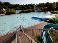 Blaue Rutsche vor Schwimmbecken, das in der Sonne glitzert.