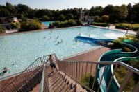 Blaue Rutsche vor Schwimmbecken, das in der Sonne glitzert.