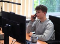 Industriekaufmann (m/w/d) Junger Mann sitzt am Schreibtisch und telefoniert.