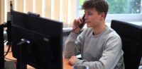 Industriekaufmann (m/w/d) Junger Mann sitzt am Schreibtisch und telefoniert.