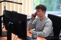 Junger Mann sitzt am Schreibtisch und telefoniert.