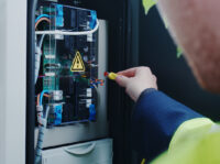 Elektroniker/Elektriker/Netzmonteur (m/w/d) im Bereich Strom Monteur arbeitet an offener Ladesäule.