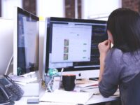 Mitarbeiter Verwaltung/Organisation (m/w/d) Frau am Schreibtisch von hinten die auf zwei Bildschirme guckt.