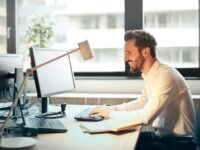 Produktmanager Commodity (m/w/d) Lachender Mann, der am Schreibtisch sitzt