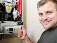 Monteur steht vor einer geöffneten Gastherme und zeigt Daumen hoch.