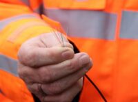 Stadtwerke Hilden und Telekom planen Zusammenarbeit beim Glasfaserausbau Eine Hand hält ein Bündel bunter Glasfasern. Die Person trägt eine orange Warnjacke.