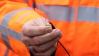 Eine Hand hält ein Bündel bunter Glasfasern. Die Person trägt eine orange Warnjacke.