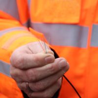 Bunte Glasfaserröhrchen in der Hand eines Monteurs in oranger Warnjacke.