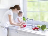 Eine Frau und ein kleines Kind stehen in der Küche und waschen Gemüse ab.