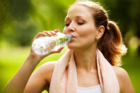 Eine sportliche Frau trinkt Wasser aus einer Flasche.