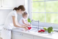 Eine Frau und ein kleines Kind stehen in der Küche und waschen Gemüse ab.